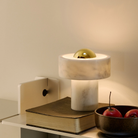 The gold Stone Cordless Lamp from Tom Dixon in a home office on top of a book on a shelf, next to a bowl.