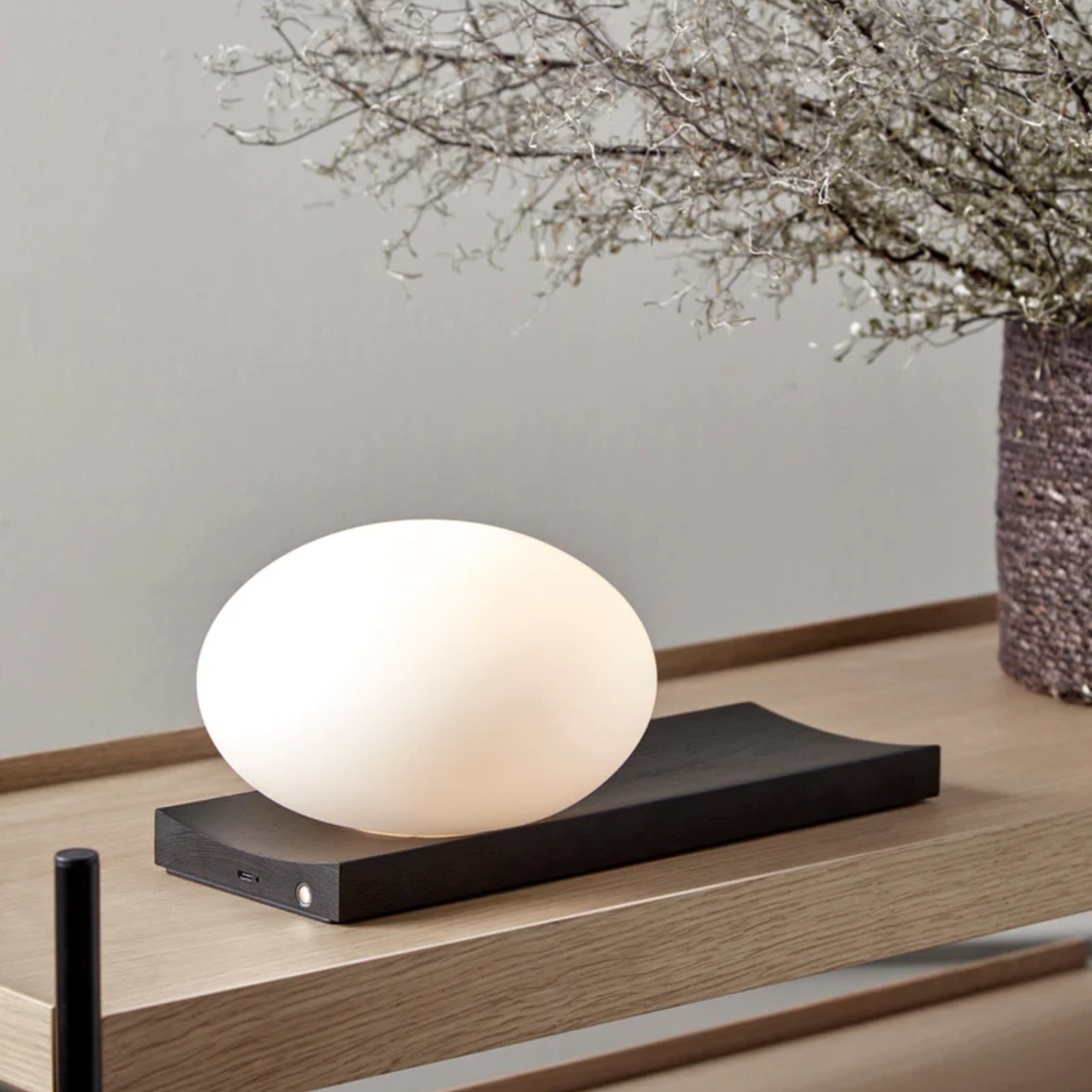 The black painted ash Dew Cordless Table Lamp & Wall Sconce from Woud in a living room.