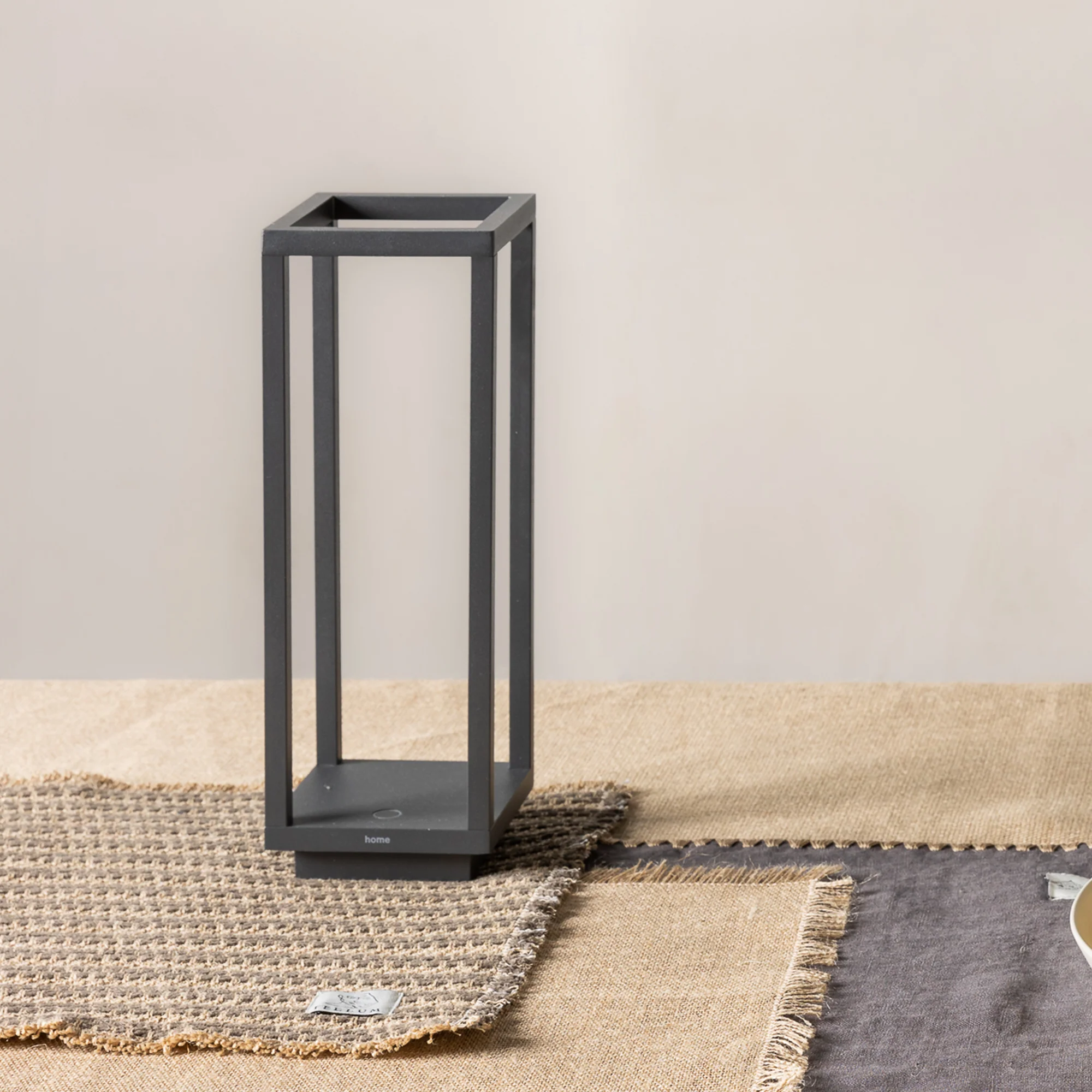 The dark gray Home Cordless Lamp from Zafferano on a dining room table on top of a placemat.