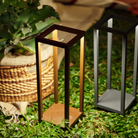 The rust Home Cordless Lamp from Zafferano in a garden next to a plant.