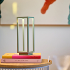The sage Home Cordless Lamp from Zafferano in a living space on top of a stack of books on an end table.