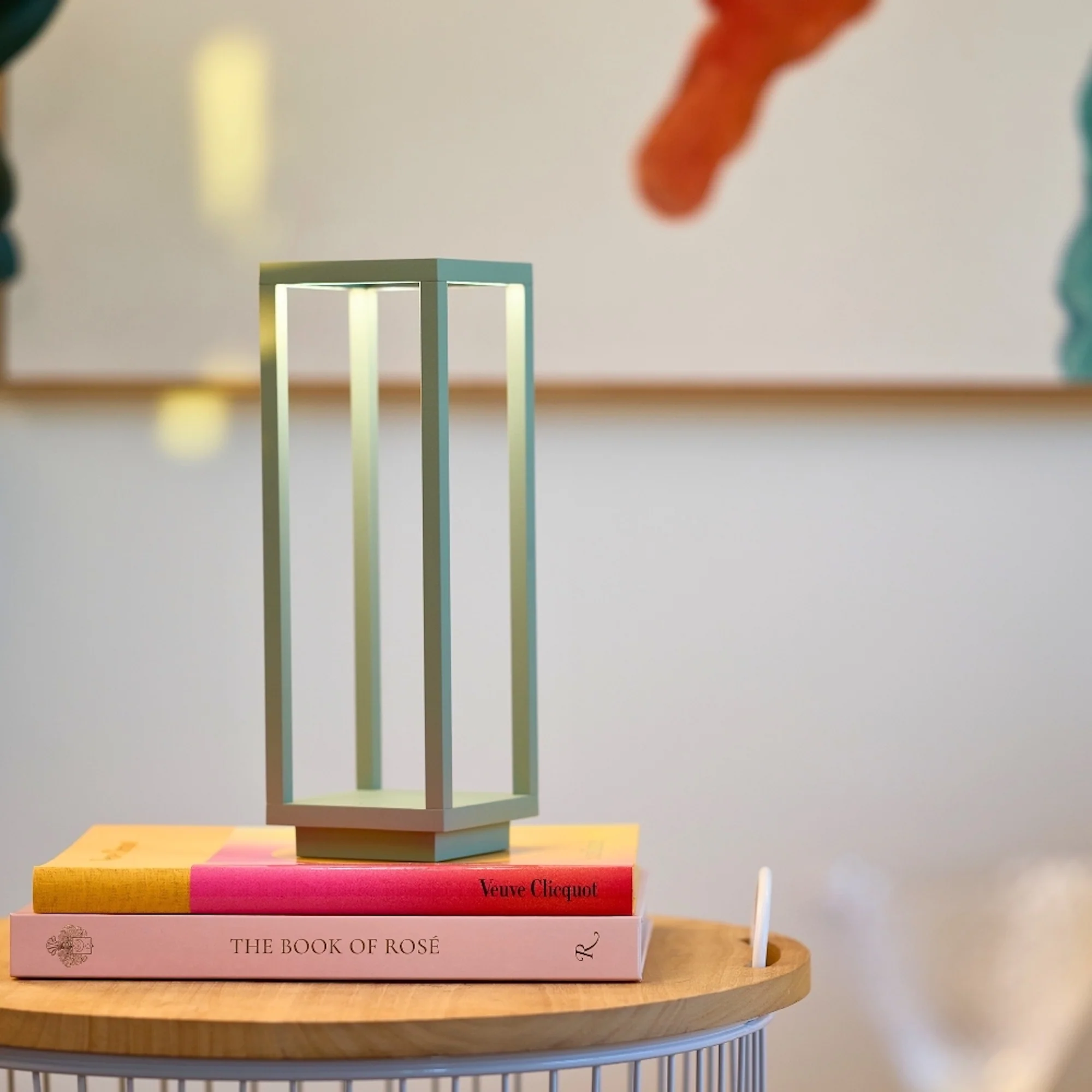The sage Home Cordless Lamp from Zafferano in a living space on top of a stack of books on an end table.