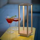 The sand Home Cordless Lamp from Zafferano in a living room on an end table next to some drinks.