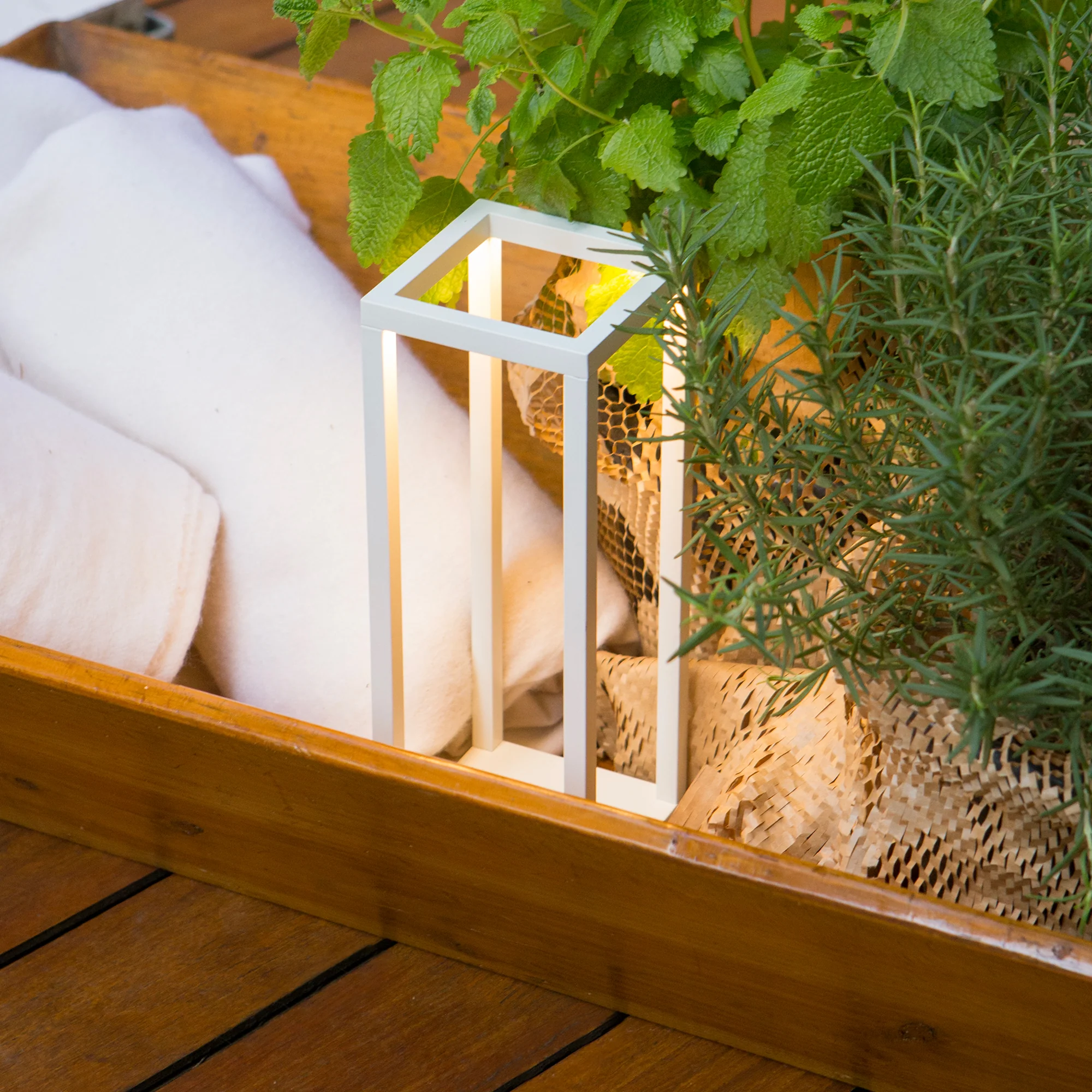The white Home Cordless Lamp from Zafferano on a pool patio next to some towels and herbs.