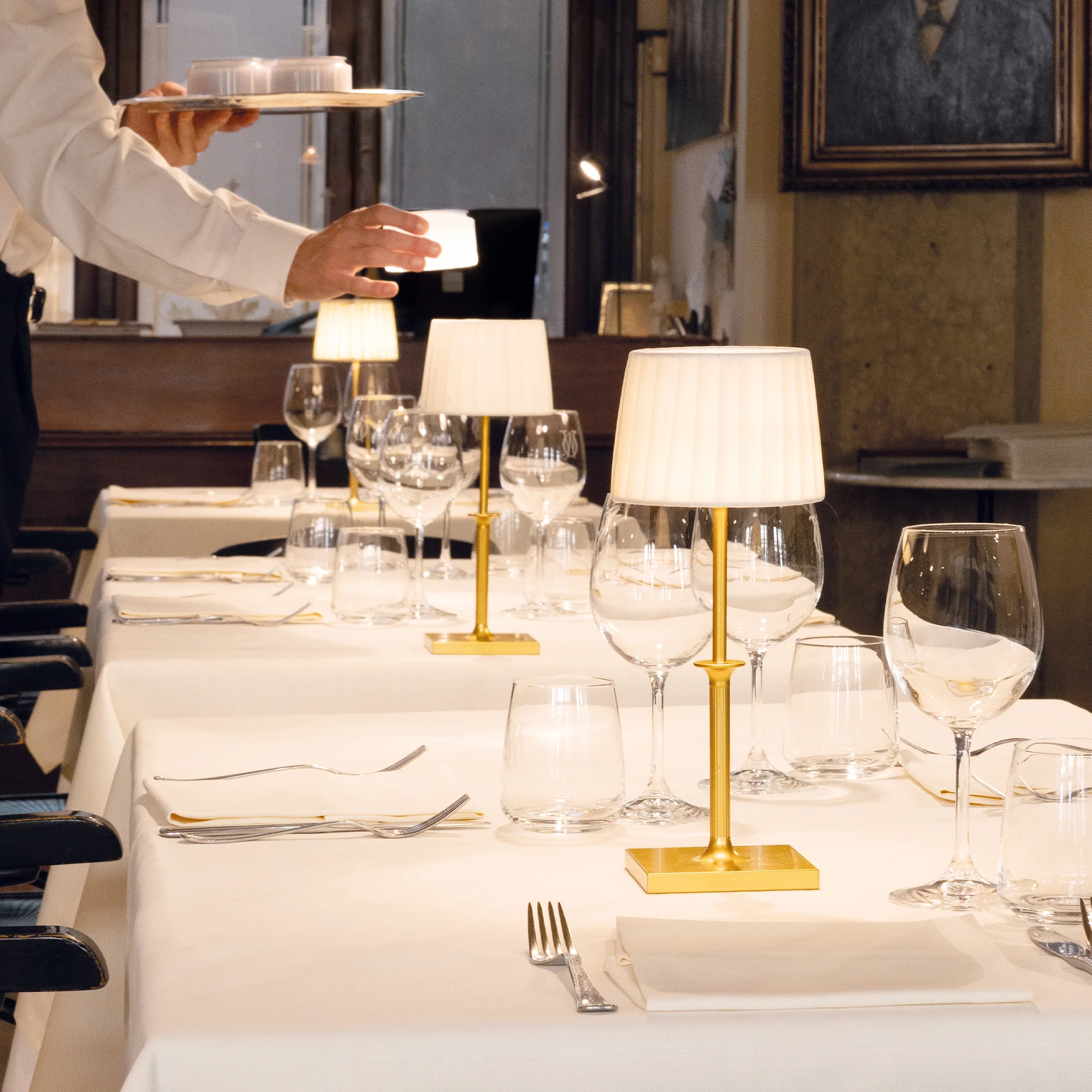 The matte gold Poldina Classic Cordless Lamp from Zafferano in a high end restaurant in the center of multiple dining tables.