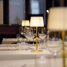 The matte gold Poldina Classic Cordless Lamp from Zafferano in a luxury cafe on top of a table with glasses.