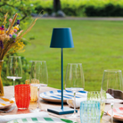 The avio blue Poldina Pro from Zafferano in a garden on a dining table with glasses and dishes.