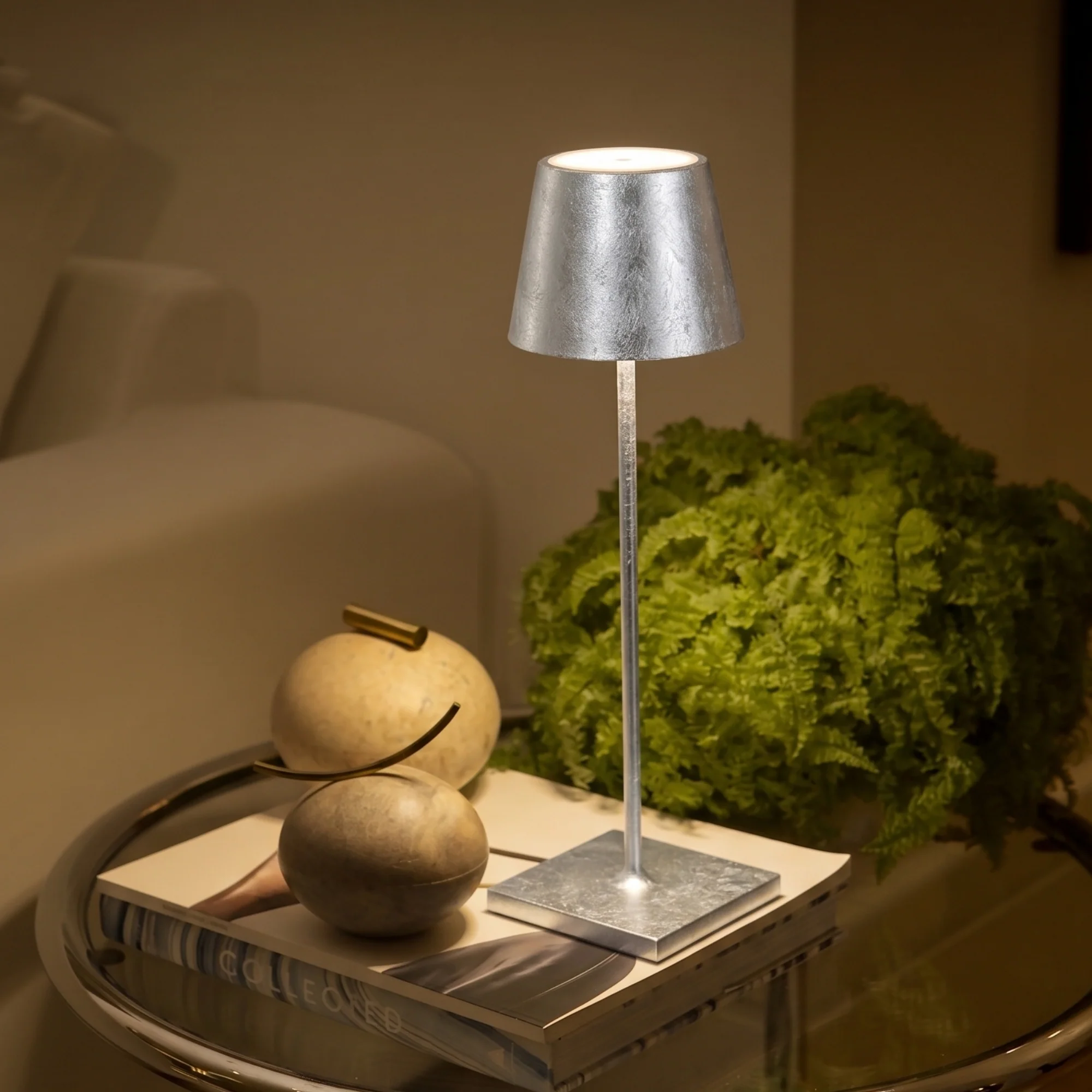 The silver leaf Poldina Pro from Zafferano in a luxury home on a glass end table next to a sofa.