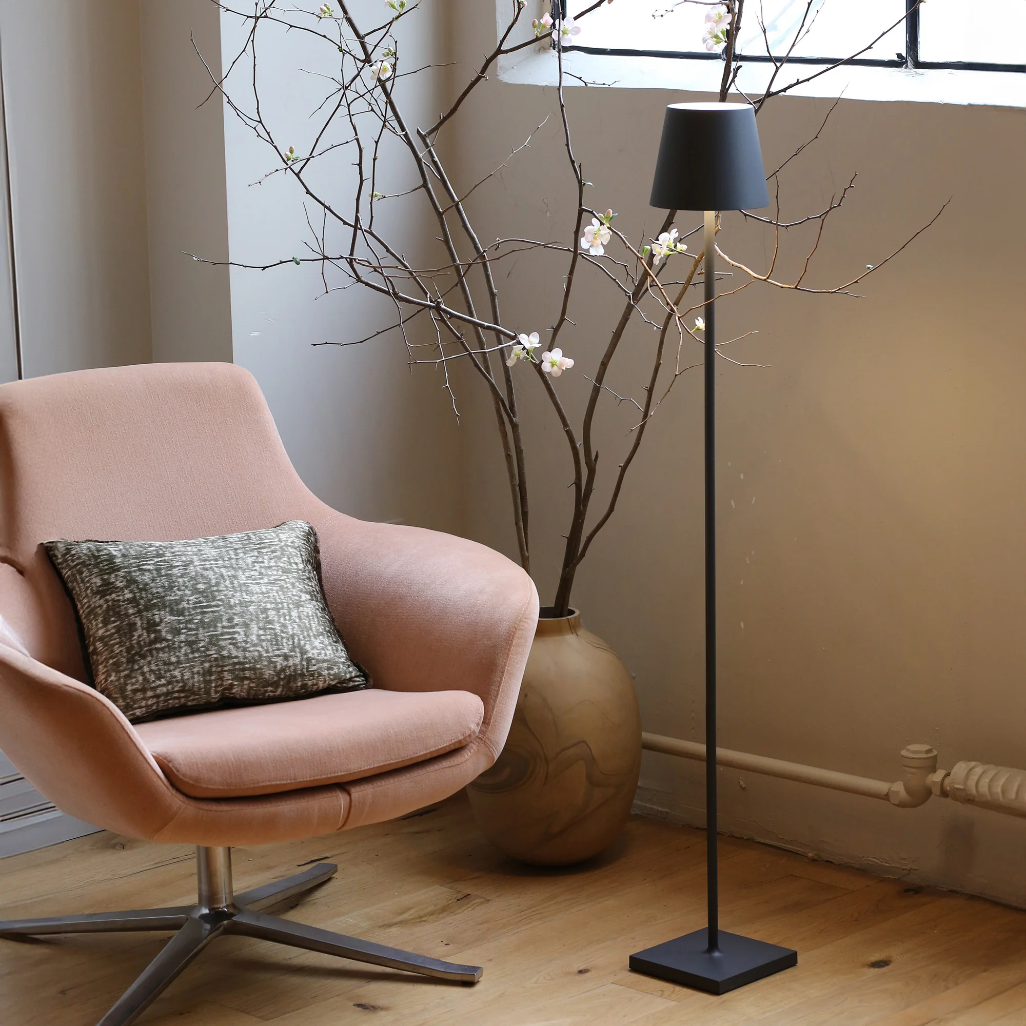 The dark gray Poldina Pro L Floor Lamp from Zafferano in a lounge beside a vase and a chair.