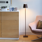 The rust Poldina Pro L Floor Lamp from Zafferano in a primary bedroom beside a cabinet and lounge chair.