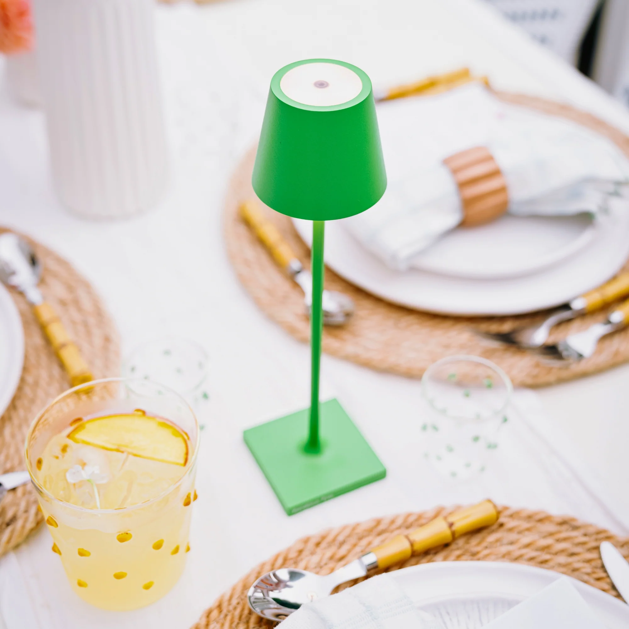 The apple green Poldina Pro Micro Cordless Lamp from Zafferano on a dining table with glasses, plates and cutlery.