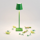 The apple green Poldina Pro Micro Cordless Lamp from Zafferano in a studio with various candies.