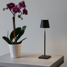 The black Poldina Pro Micro Cordless Lamp from Zafferano used on a table in a hospitality setting.