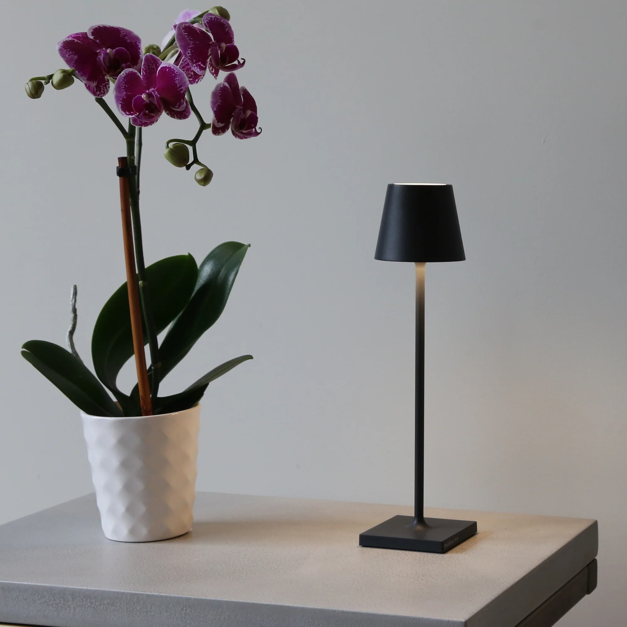 The black Poldina Pro Micro Cordless Lamp from Zafferano used on a table in a hospitality setting.