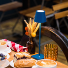 The capri blue Poldina Pro Micro Cordless Lamp from Zafferano on top of a table at a bakery.