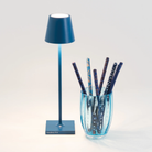 The capri blue Poldina Pro Micro Cordless Lamp from Zafferano in a studio beside a cup.