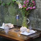 The dark gray Poldina Pro Micro Cordless Lamp from Zafferano on top of a live wooden table in a cafe.