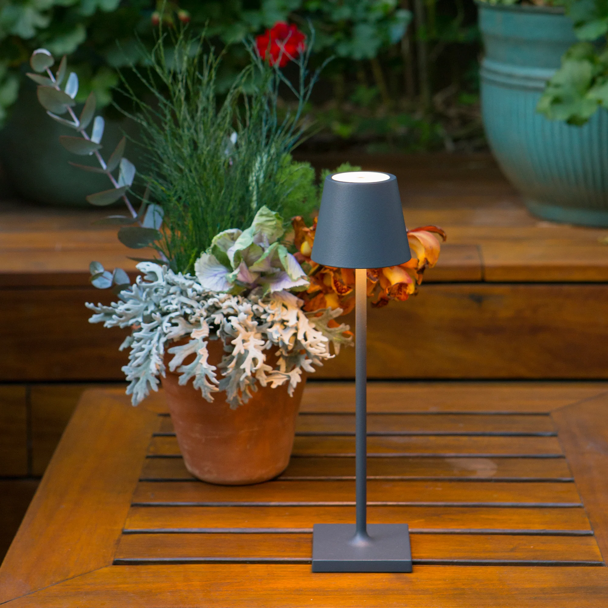 The dark gray Poldina Pro Micro Cordless Lamp from Zafferano in a living area on top of a wooden table.