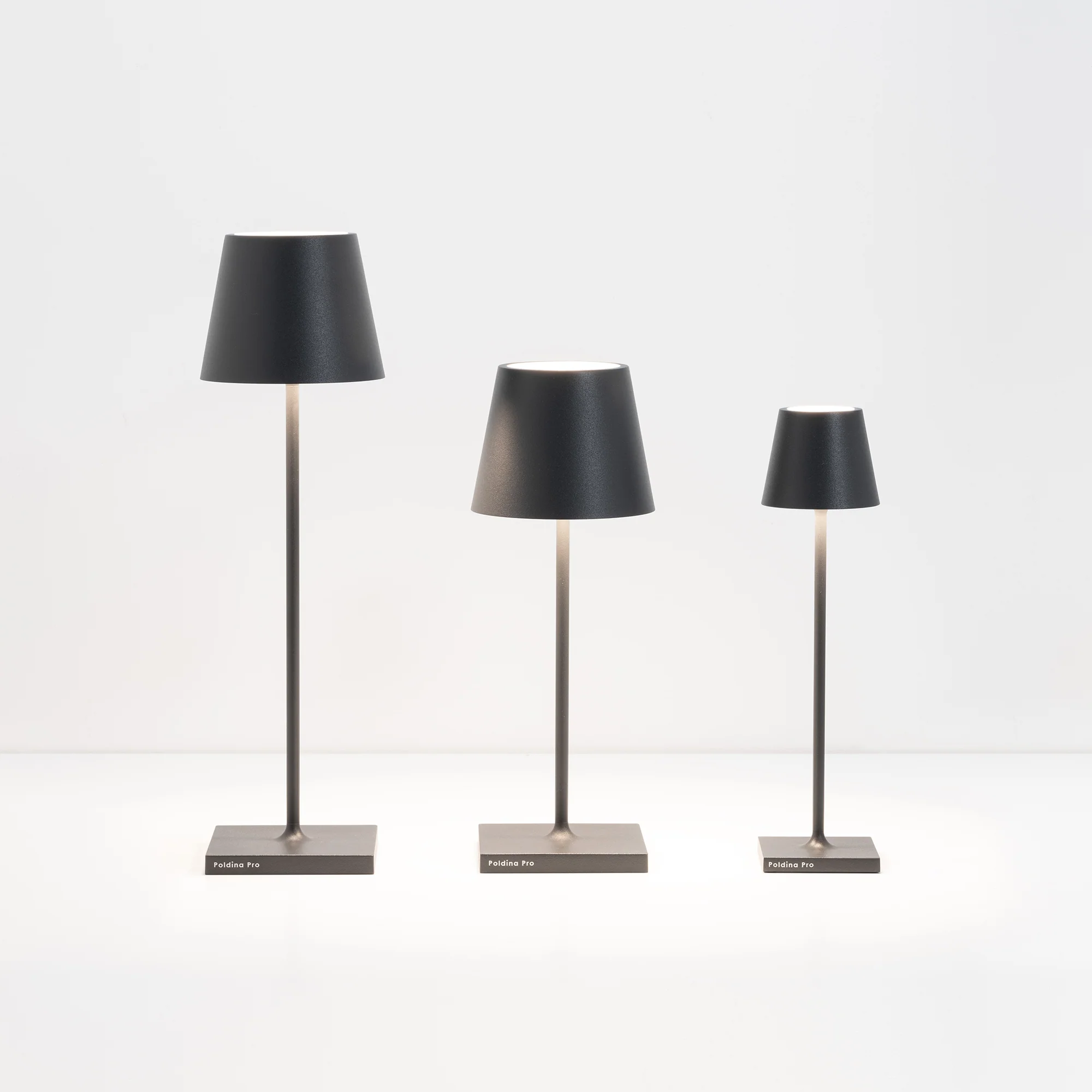 The dark gray Poldina Pro Micro Cordless Lamp from Zafferano alongside the other Poldina sizes.