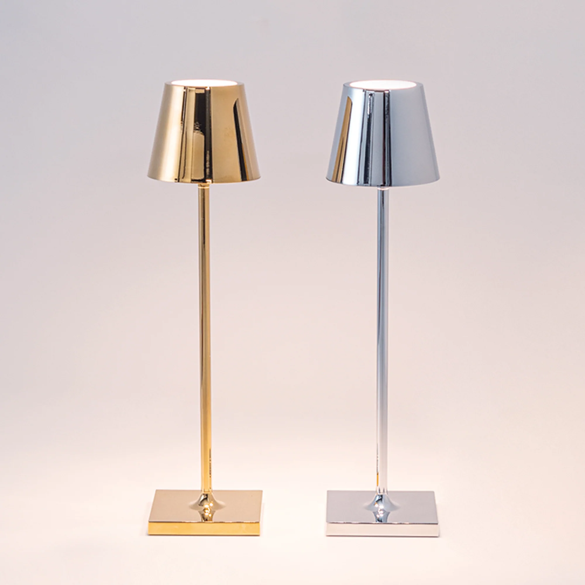The glossy chrome Poldina Pro Micro Cordless Lamp from Zafferano next to the glossy gold Poldina Pro Micro Portable Lamp in a studio.