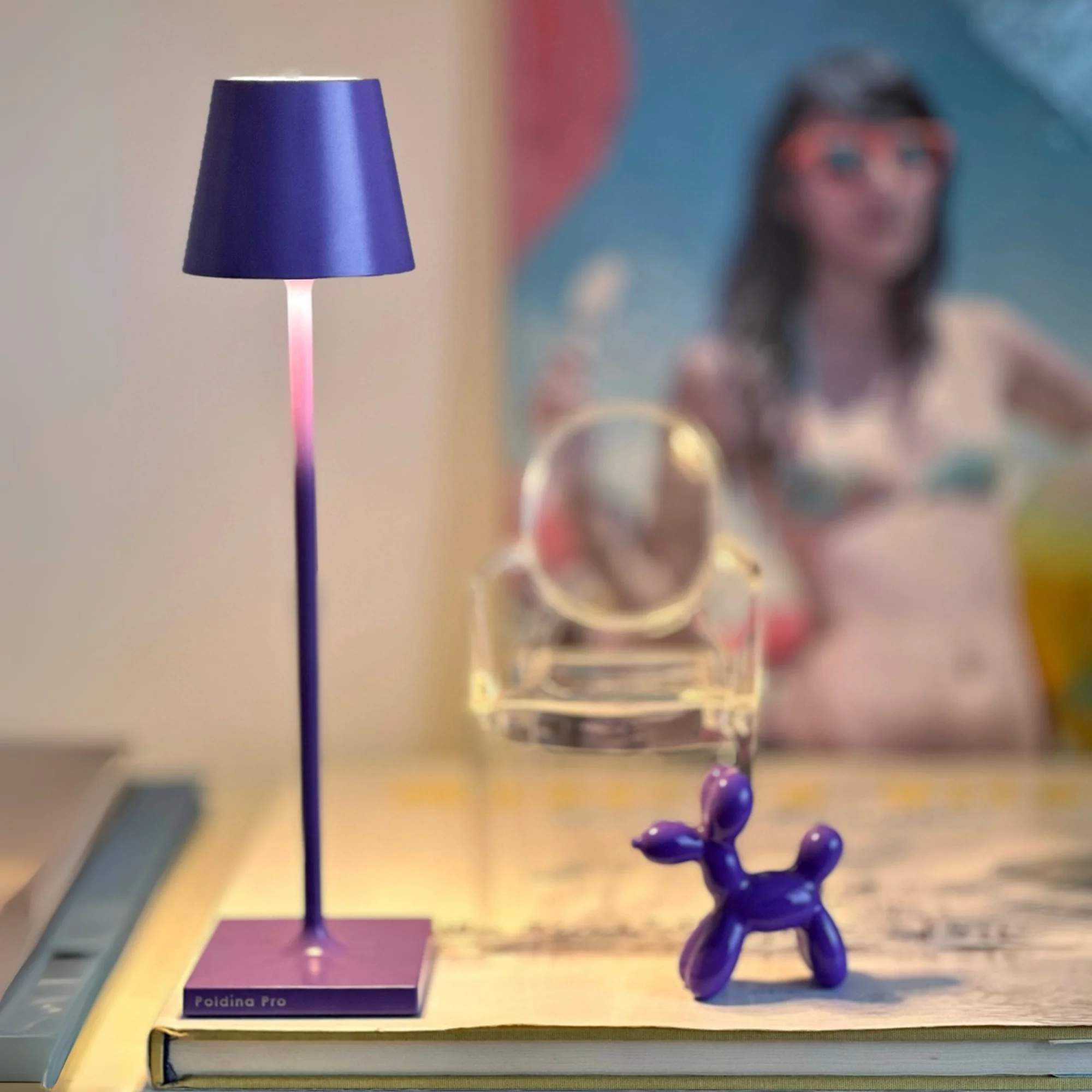 The lilac Poldina Pro Micro Cordless Lamp from Zafferano in a lounge surrounded by decor.