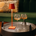 The red Poldina Pro Micro Cordless Lamp from Zafferano in a living room on top of an end table.