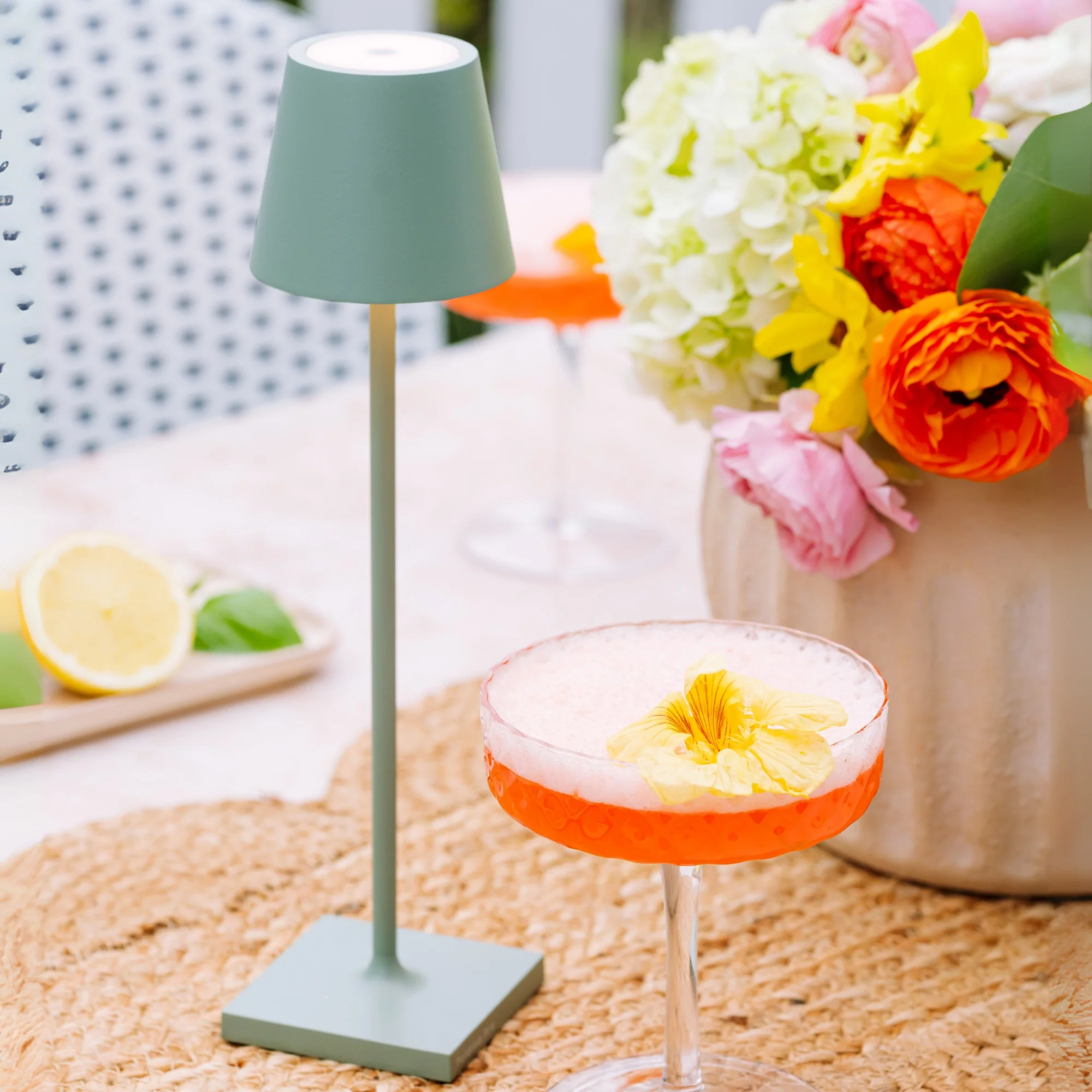 The sage Poldina Pro Micro Cordless Lamp from Zafferano at a wet bar next to a cocktail.