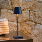 The steel blue Poldina Pro Micro Cordless Lamp from Zafferano in a living space on top of a table.