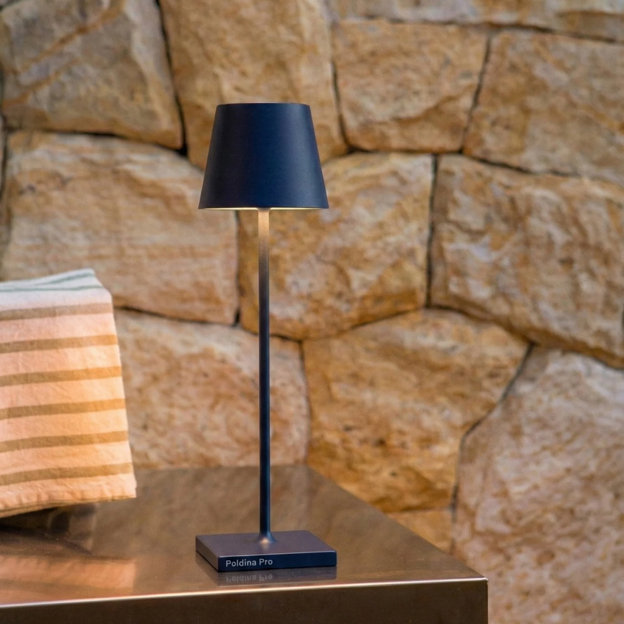 The steel blue Poldina Pro Micro Cordless Lamp from Zafferano in a living space on top of a table.