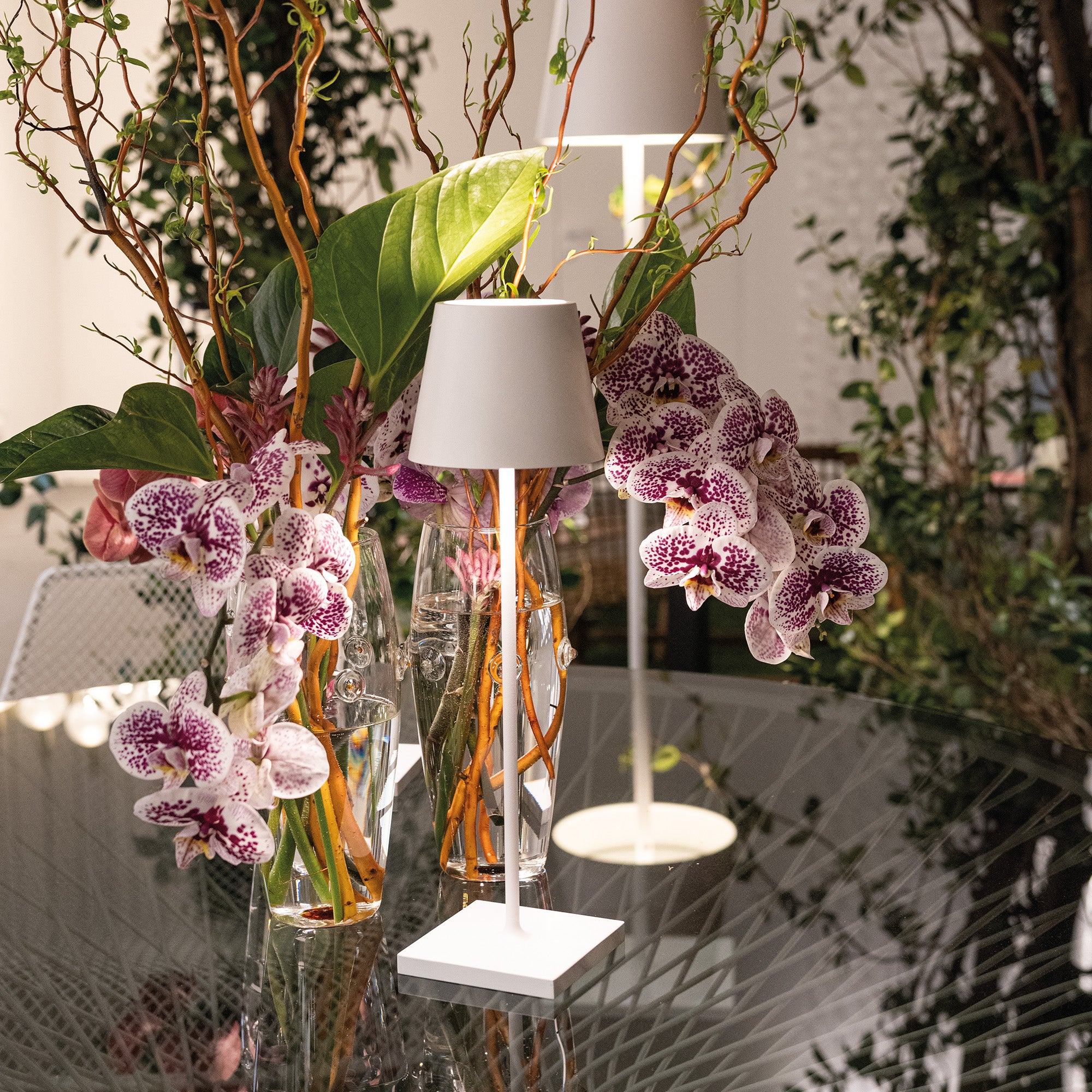 The white Poldina Pro Micro Cordless Lamp from Zafferano on top of a glass entryway table with flowers.