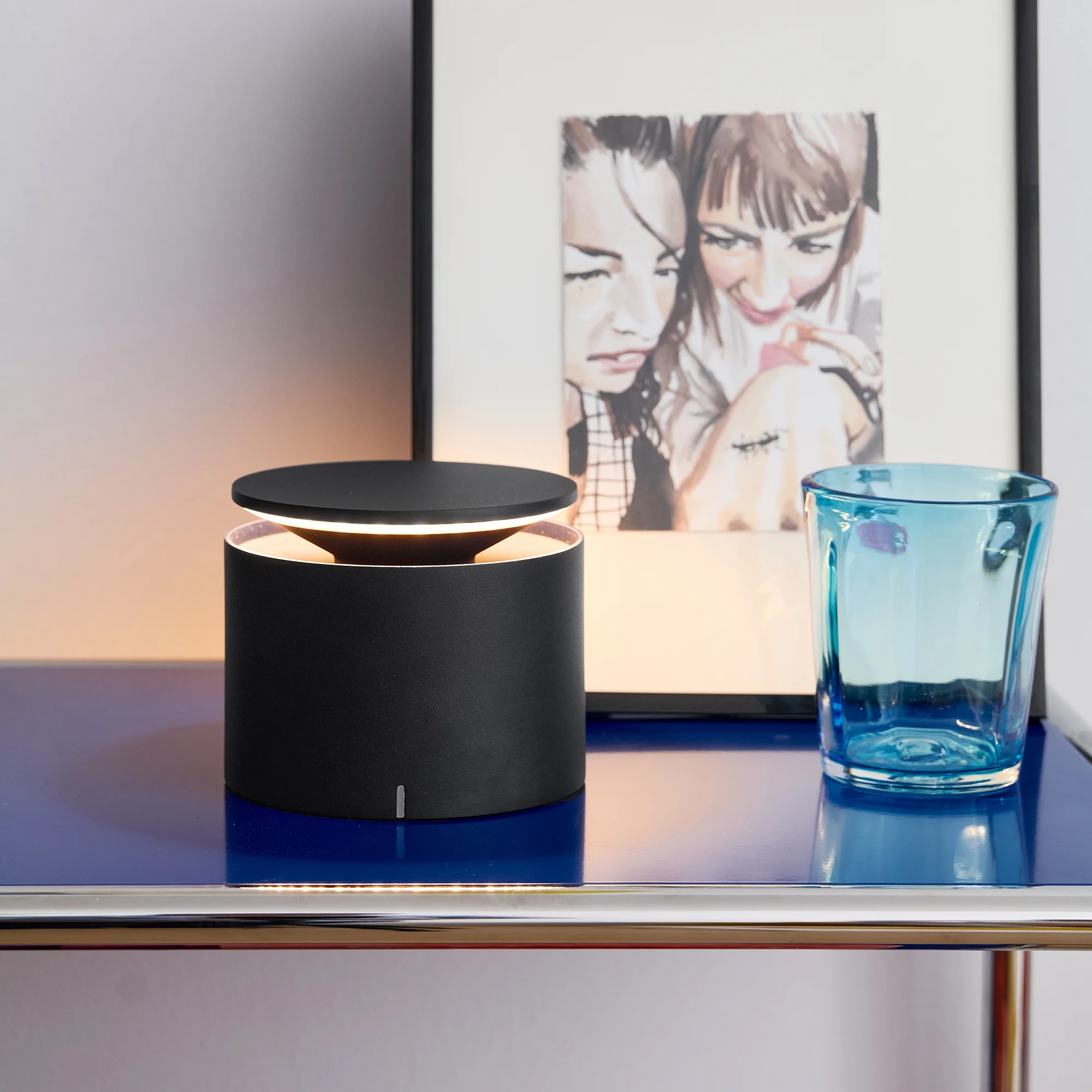 The dark grey PushUp Pro Cordless Lamp from Zafferano in a living room beside a family painting on a shelf.