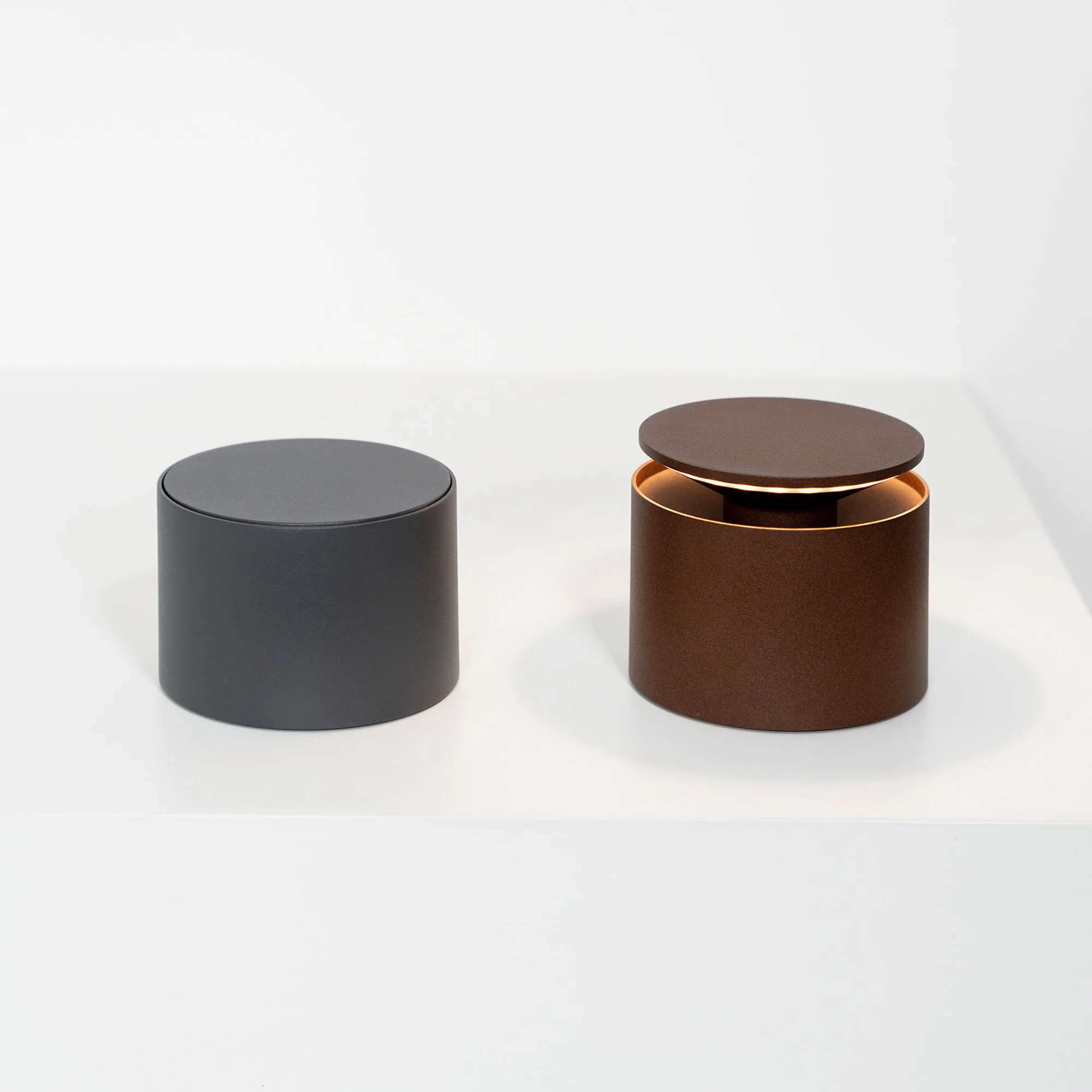 The rust PushUp Pro Cordless Lamp from Zafferano with the dark grey PushUp Pro in a living space on a white table.