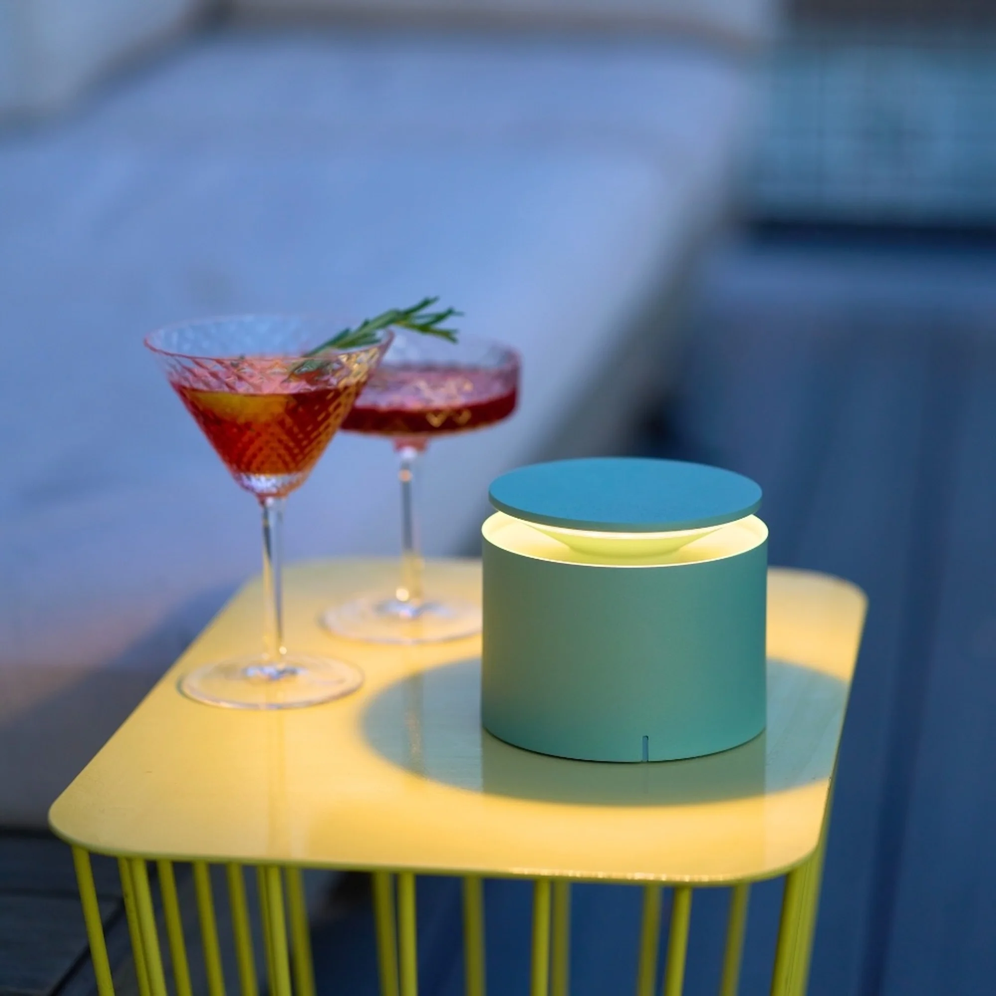 The sage PushUp Pro Cordless Lamp from Zafferano in an outdoor dining setting on top of a cafe table.
