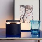 The steel blue PushUp Pro Cordless Lamp from Zafferano in a primary bedroom next to a painting and glass.