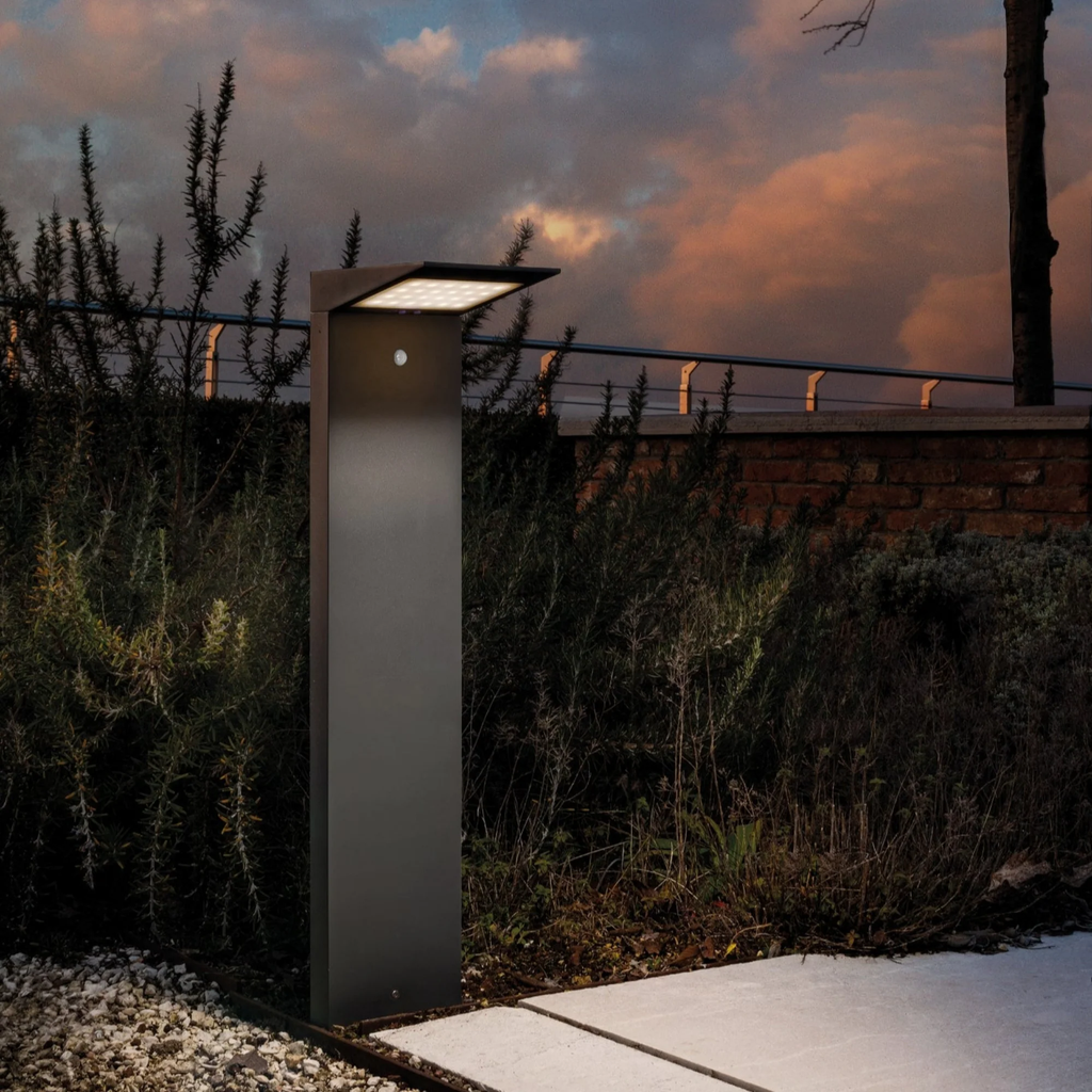 The dark gray Solar Outdoor LED Bollard from Zafferano outdoors beside a pathway.