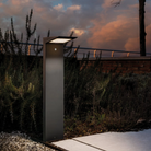 The dark gray Solar Outdoor LED Bollard from Zafferano outdoors beside a pathway.