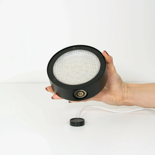 The black Super O Wall Spotlight Sconce from Zafferano being charged using the charging module.