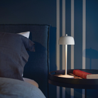 The matte white Theta Pro Cordless Lamp from Zafferano in a bedroom on a bedside table.