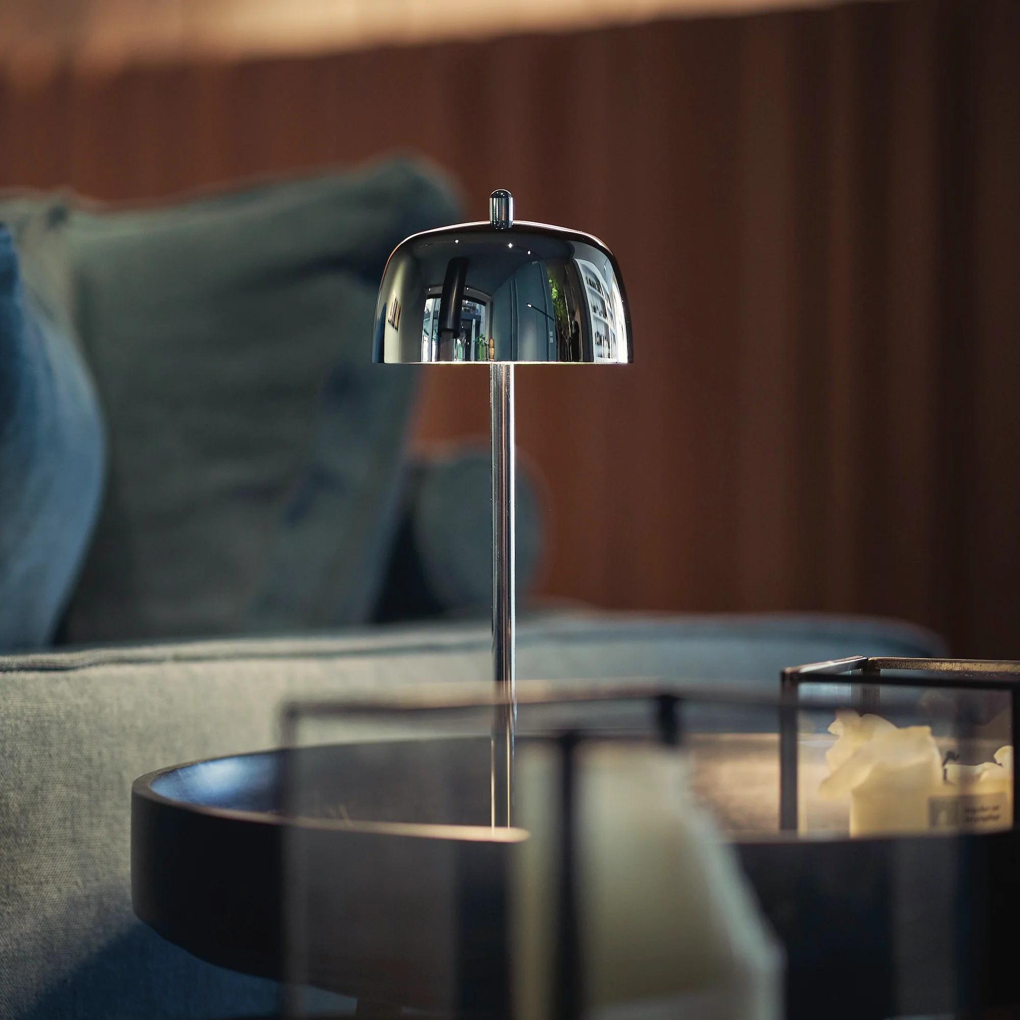 The polished chrome Theta Pro Cordless Lamp from Zafferano on an end table in a living room.