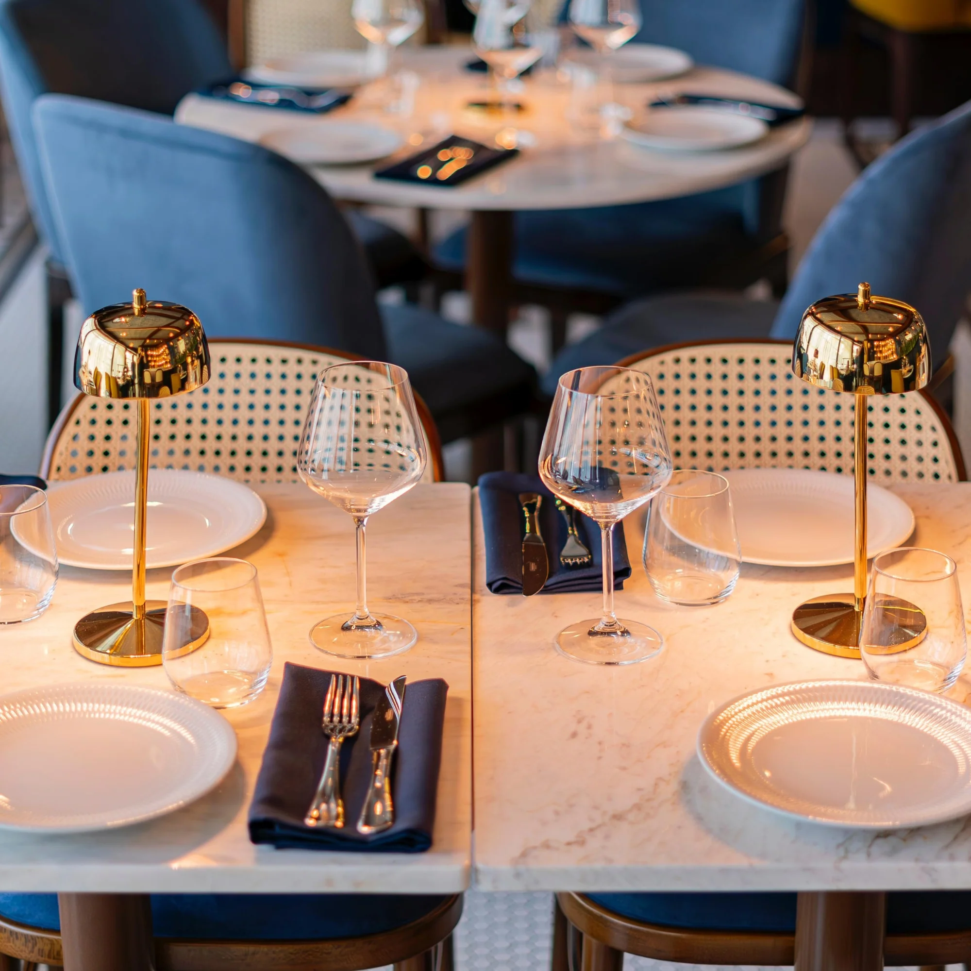 The polished gold Theta Pro Cordless Lamp from Zafferano on a marble dining table in a cafe.