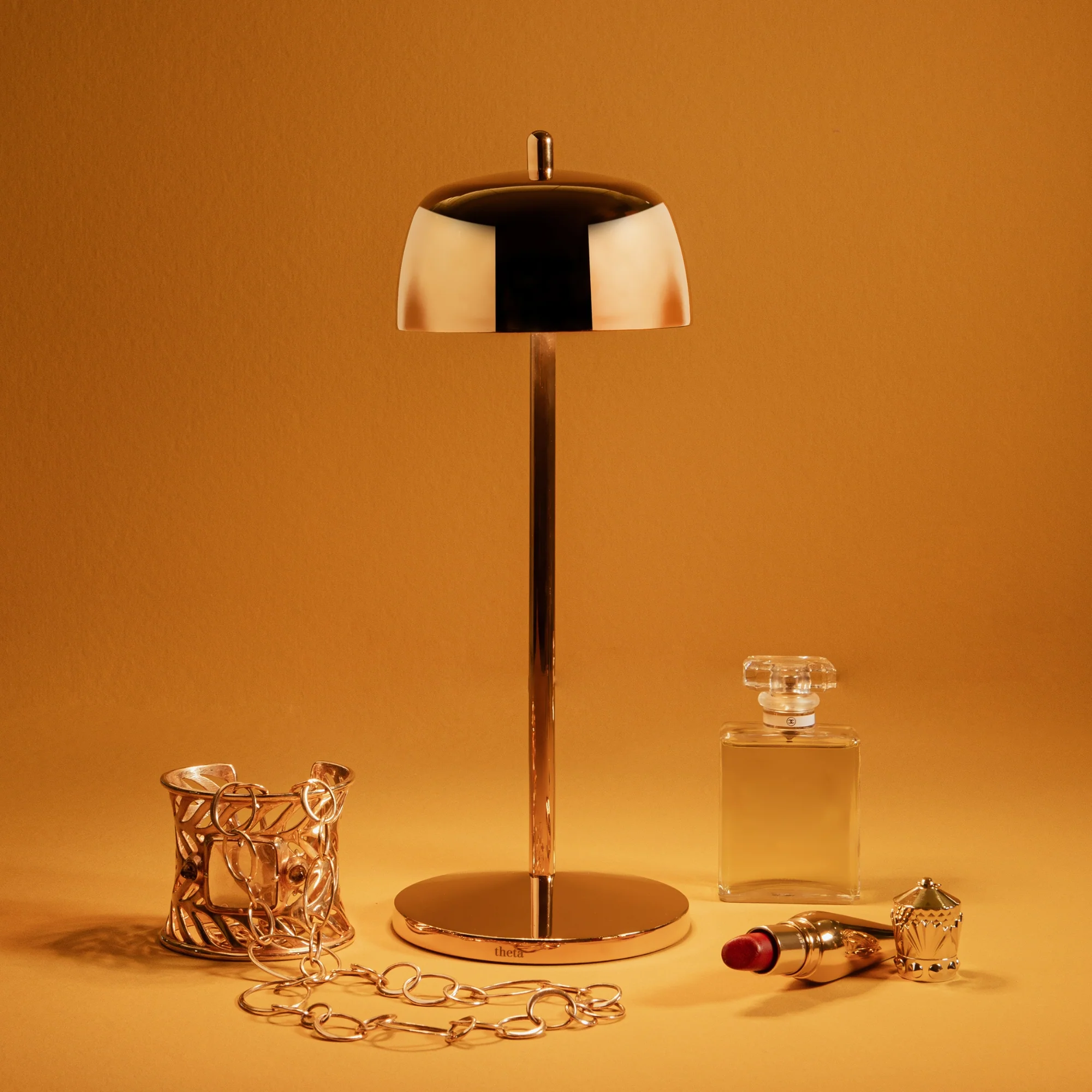 The polished gold Theta Pro Cordless Lamp from Zafferano in a studio with gold decor and jewlery.