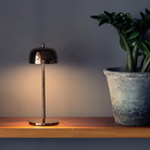 The rose gold Theta Pro Cordless Lamp from Zafferano on top of a desk in a business space.