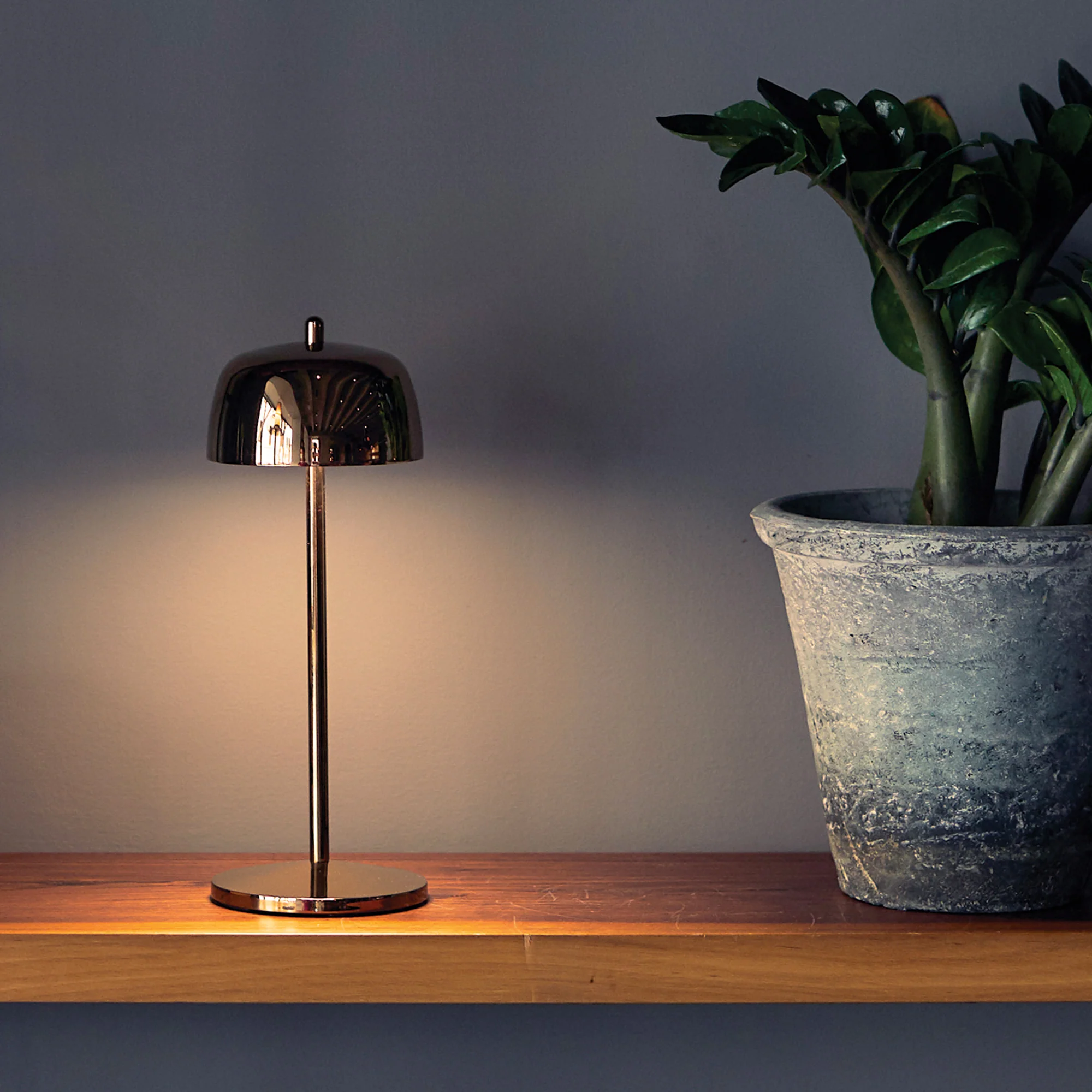 The rose gold Theta Pro Cordless Lamp from Zafferano on top of a desk in a business space.