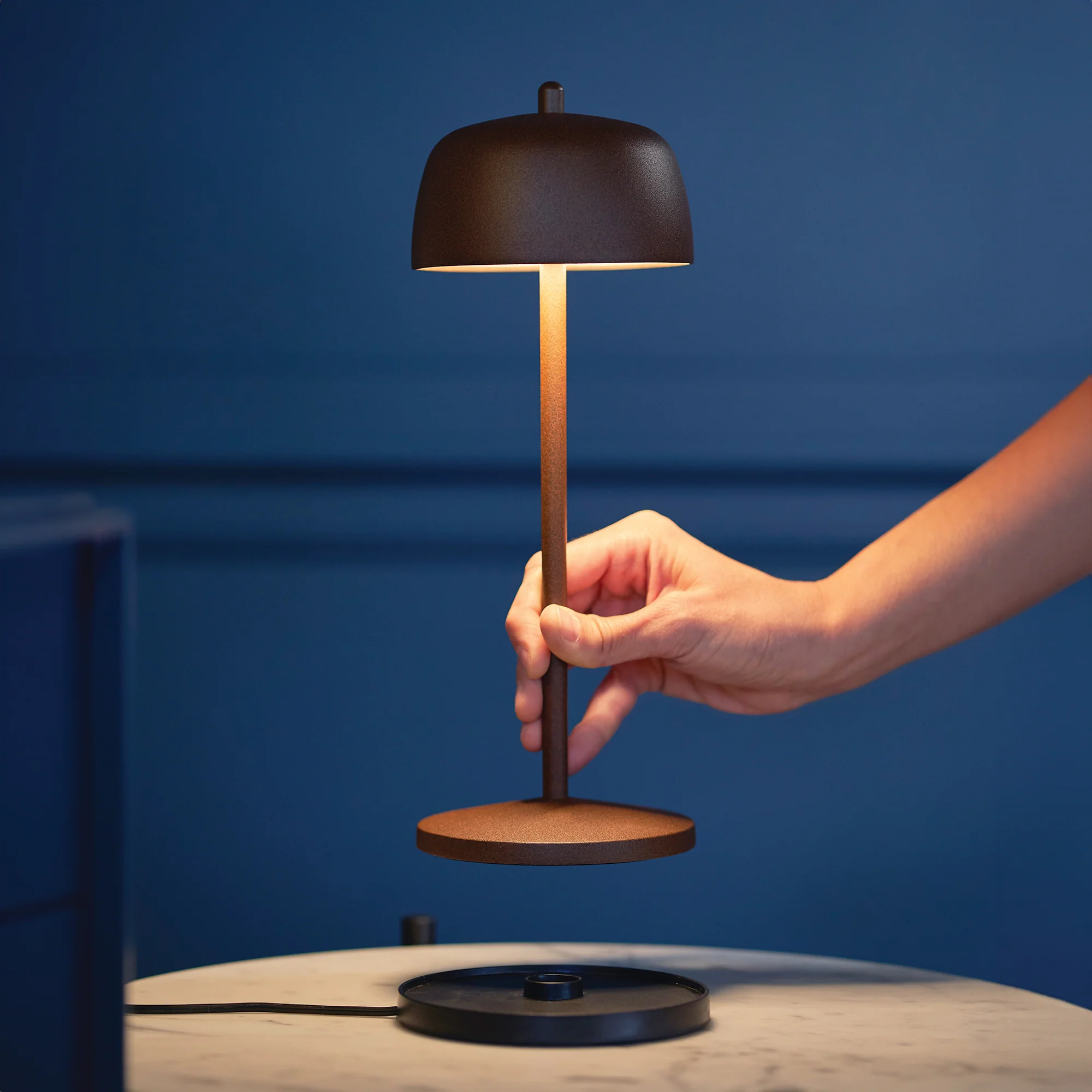 The rust Theta Pro Cordless Lamp from Zafferano in a family area, being placed on it's incldued induction charging base.